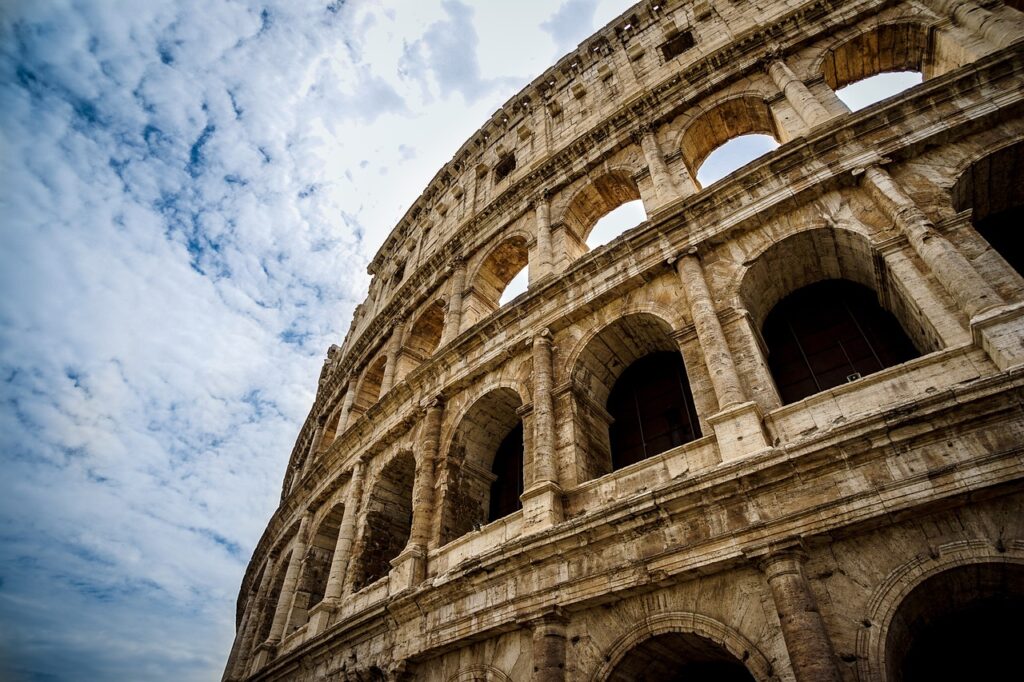 The photo shows a close-up of the Colosseum in Rome, Italy, with its ancient stone arches against a partly cloudy sky.