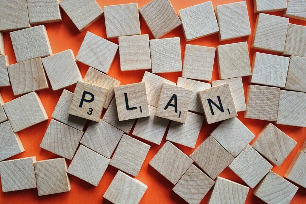 Wooden Scrabble tiles spelling "PLAN" are surrounded by blank wooden squares on an orange background.
