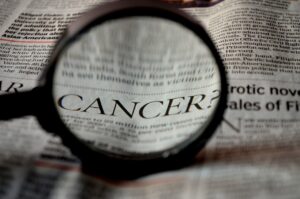 A magnifying glass focuses on the word "CANCER" in a newspaper article, highlighting the crucial role of NHS staff in advancing primary care.