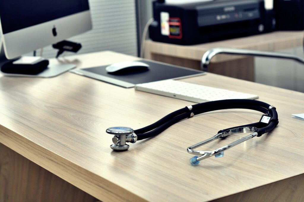 A stethoscope rests on an empty doctors desk next to a computer in the office, a familiar scene for NHS staff working tirelessly to support GPs.