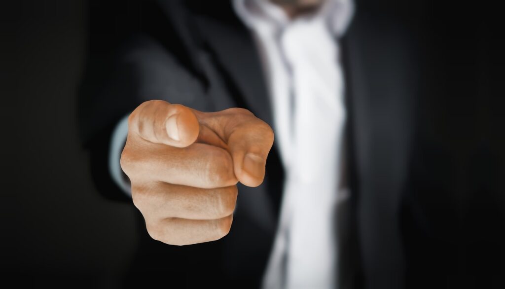 A person in a suit points directly at the camera against a dark background, embodying the urgency of addressing hospital waiting times and supporting dedicated nurses.