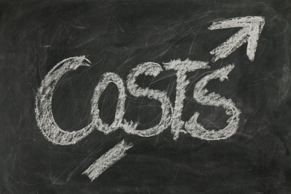 The word "costs" is written in large chalk letters on a blackboard, with an upward pointing arrow above it, suggesting rising costs—a challenge hospitals like the NHS face while seeking ways of cutting costs.