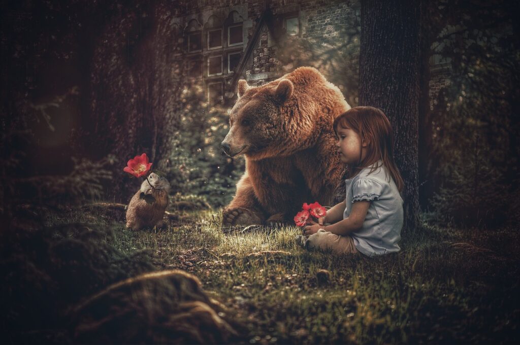 A young girl sits on grass next to a bear and a small animal holding a red flower in a forest clearing with an old building in the background.