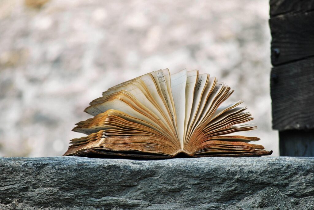 An old, weathered book with curling pages open on a stone surface.