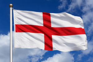 The St George's Cross flag of England billows dramatically in the wind against a bright blue sky with scattered white clouds, symbolising English identity, pride and national heritage. NHS leadership and organisational culture